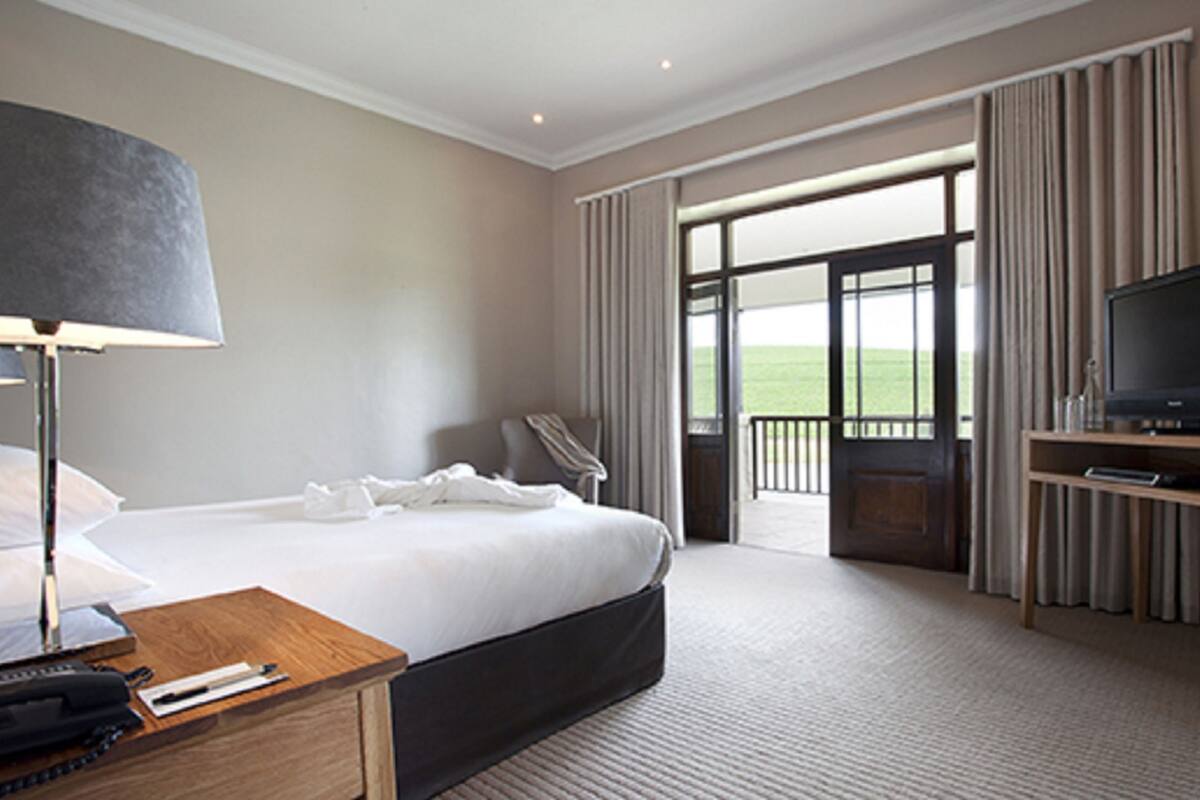 A hotel room with a large bed, a desk with a lamp, a television, and a view of the outdoors.
