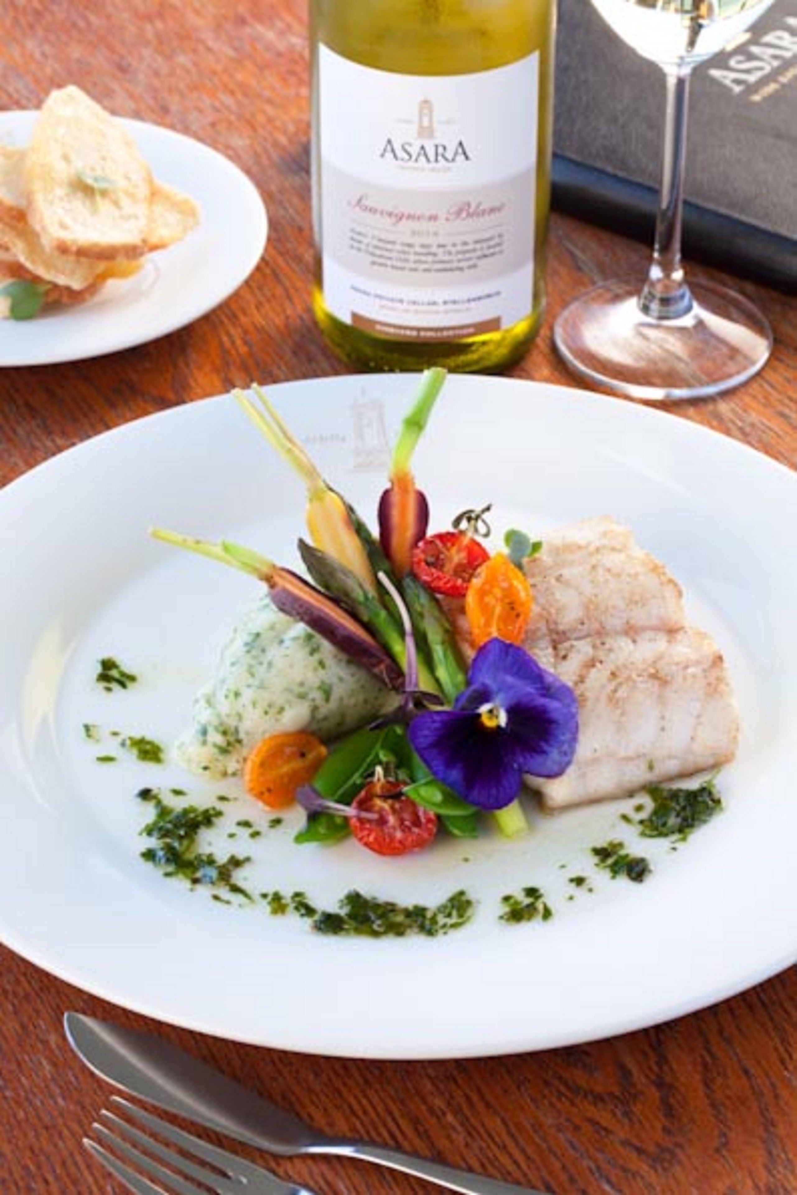 A plate of food with a bottle of Asara wine and a glass of wine on a wooden table.