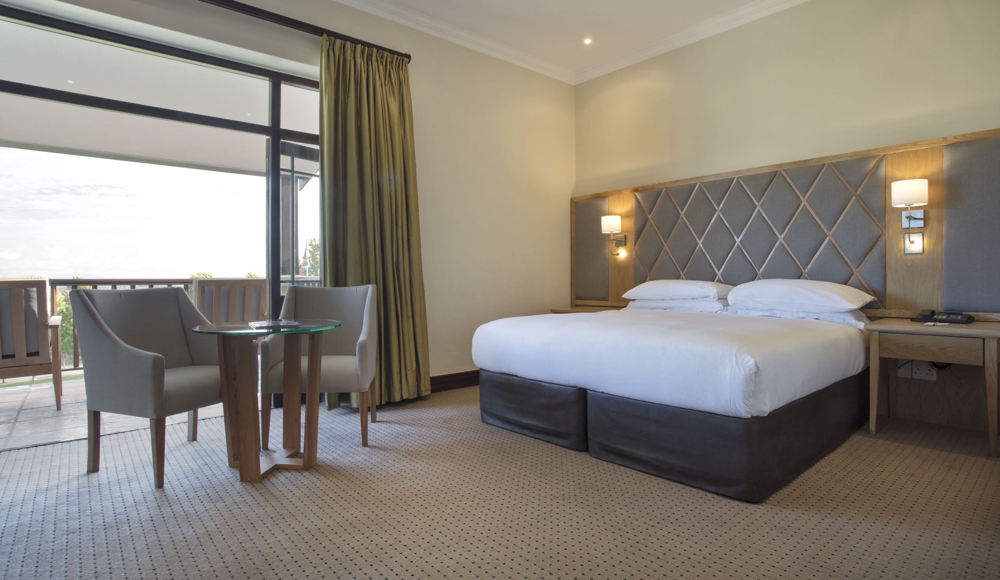 A hotel room with a large bed, a desk, a chair, and a balcony with a view.
