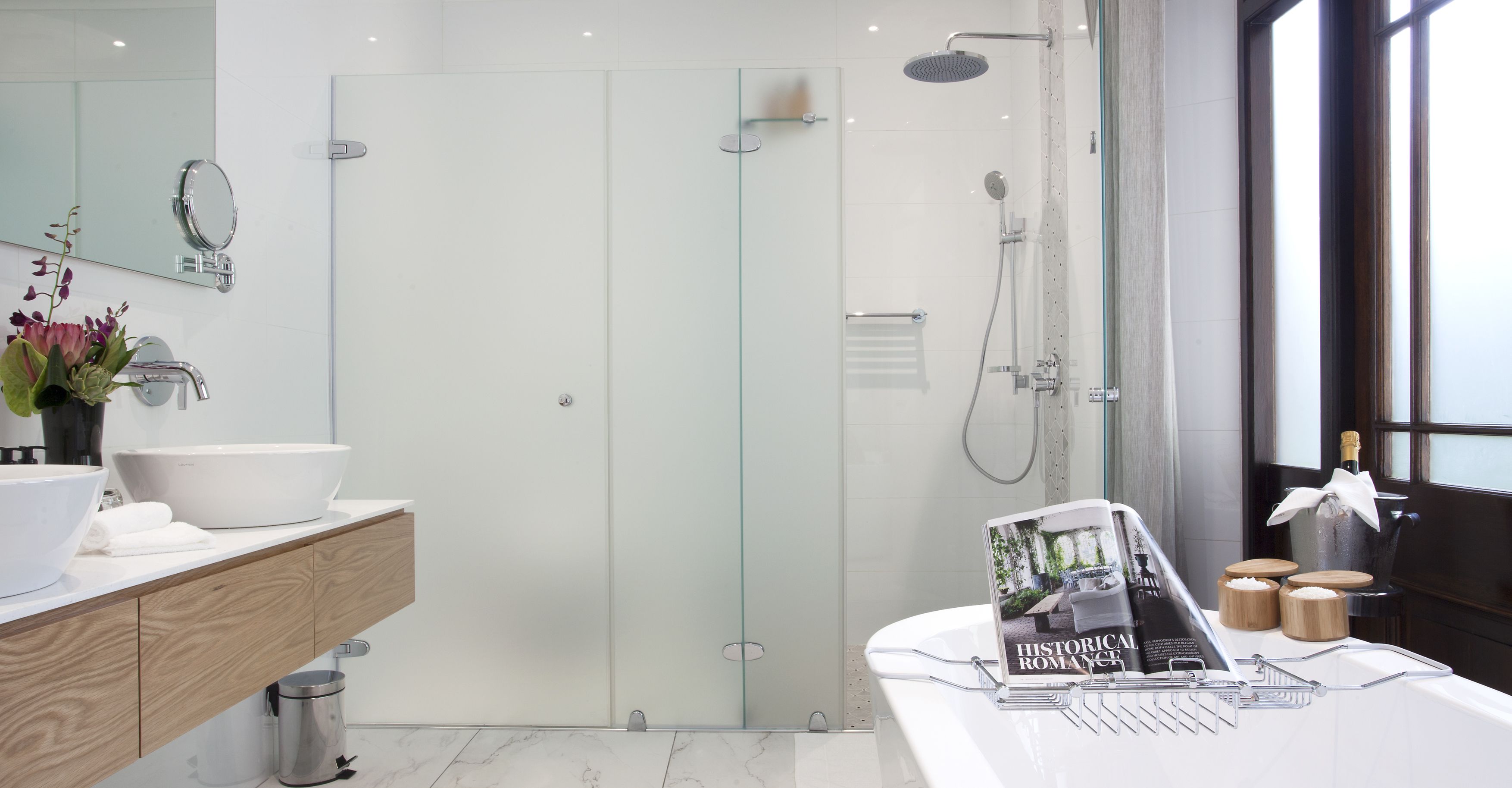 A modern bathroom with a glass-enclosed shower, a large white sink, and a magazine on the vanity.