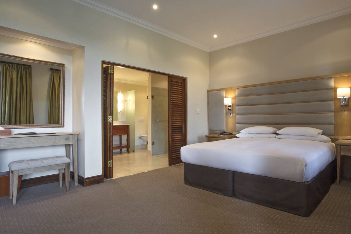 A hotel room with a large bed, bedside tables, a desk, and a mirror.