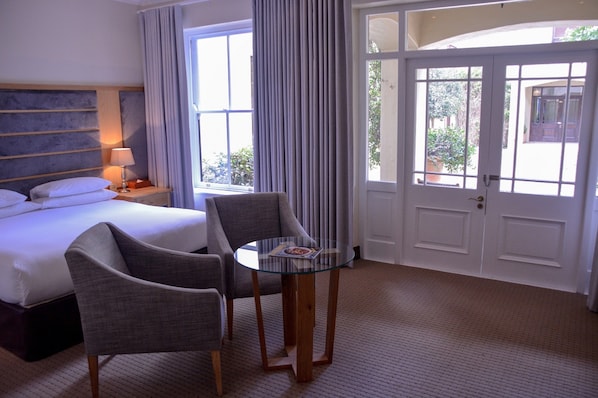 A hotel room with a bed, two chairs, a glass table, and a door leading to an outdoor area. - Asara Wine Estate & Hotel (Stellenbosch)