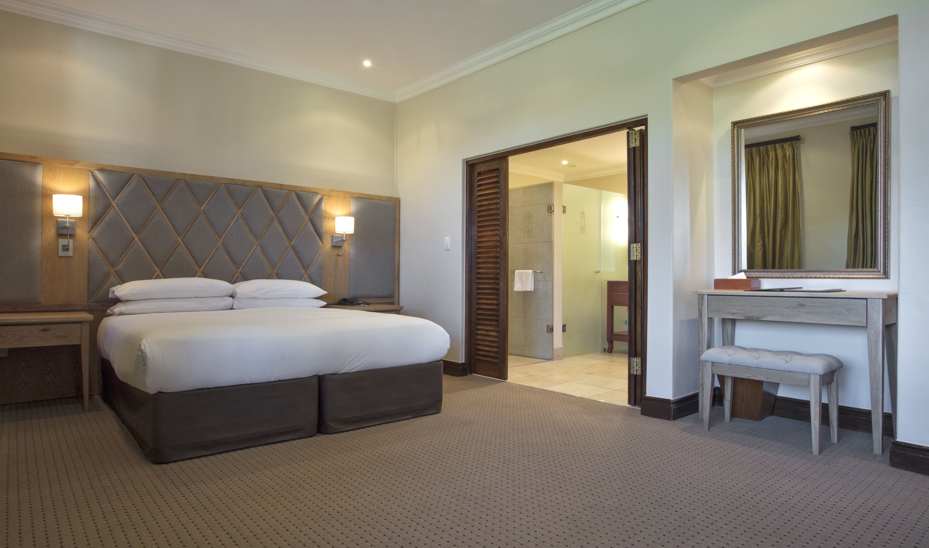 A hotel room with a large bed, a bedside table, a mirror, and a door leading to another room.
