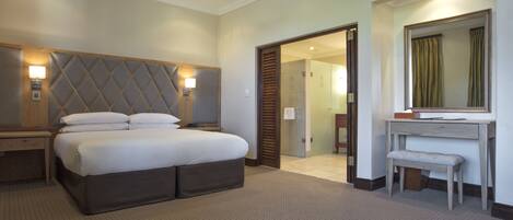 A hotel room with a large bed, a bedside table, a mirror, and a door leading to another room.