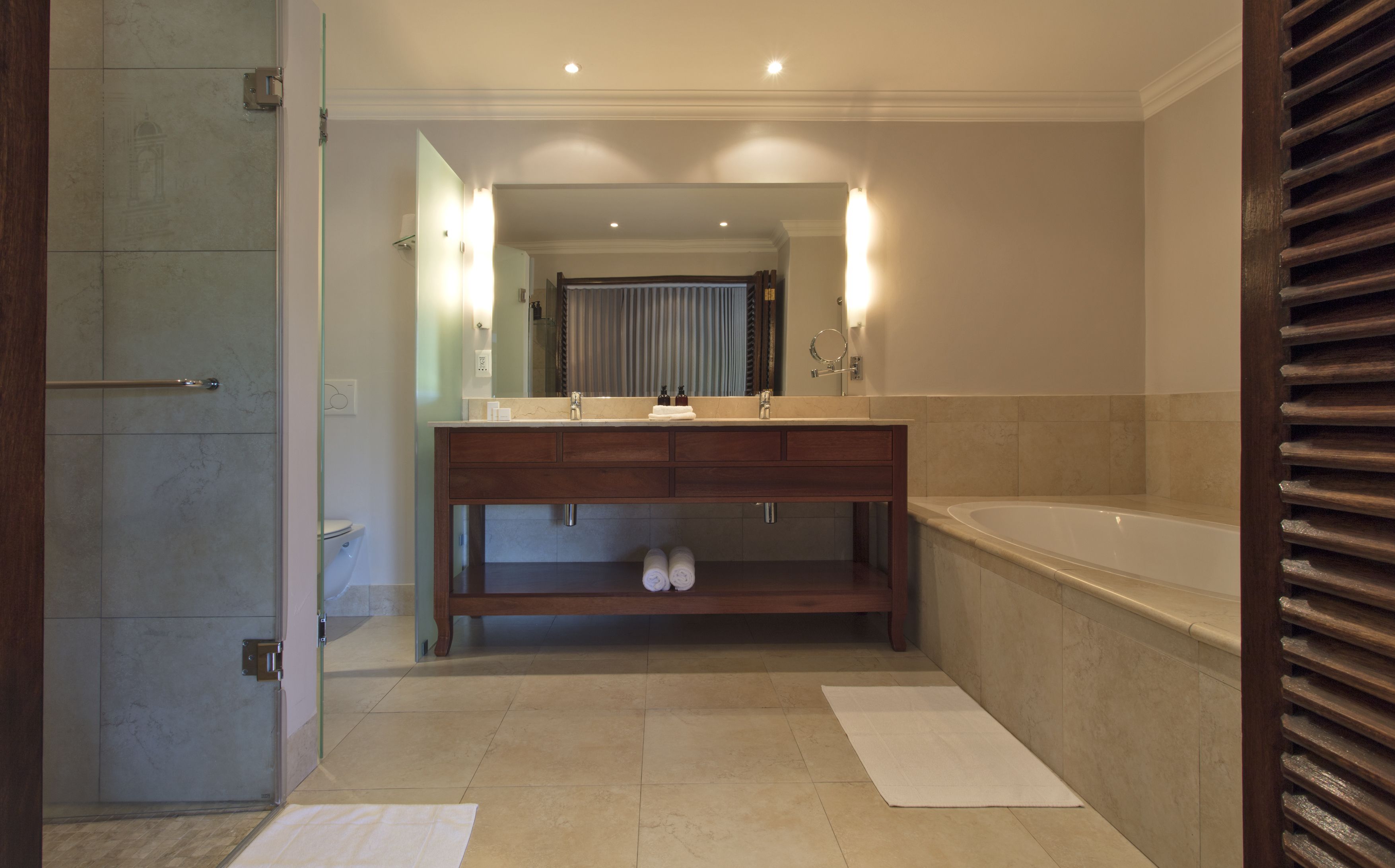 A modern bathroom with a large mirror, a wooden vanity, a bathtub, and a shower area.