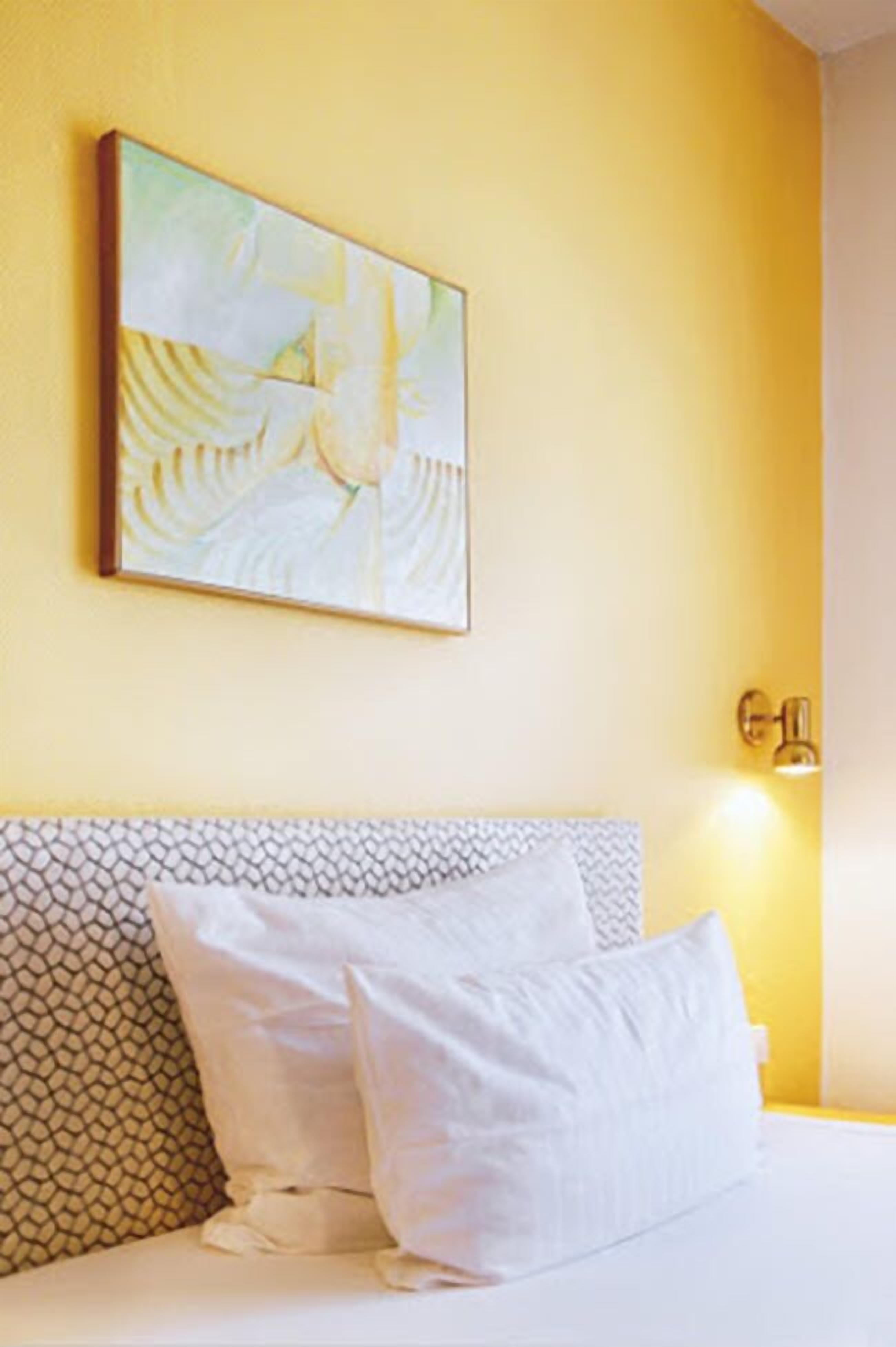 Et hotelværelse med en seng, et billede på væggen og en lampe monteret på væggen.