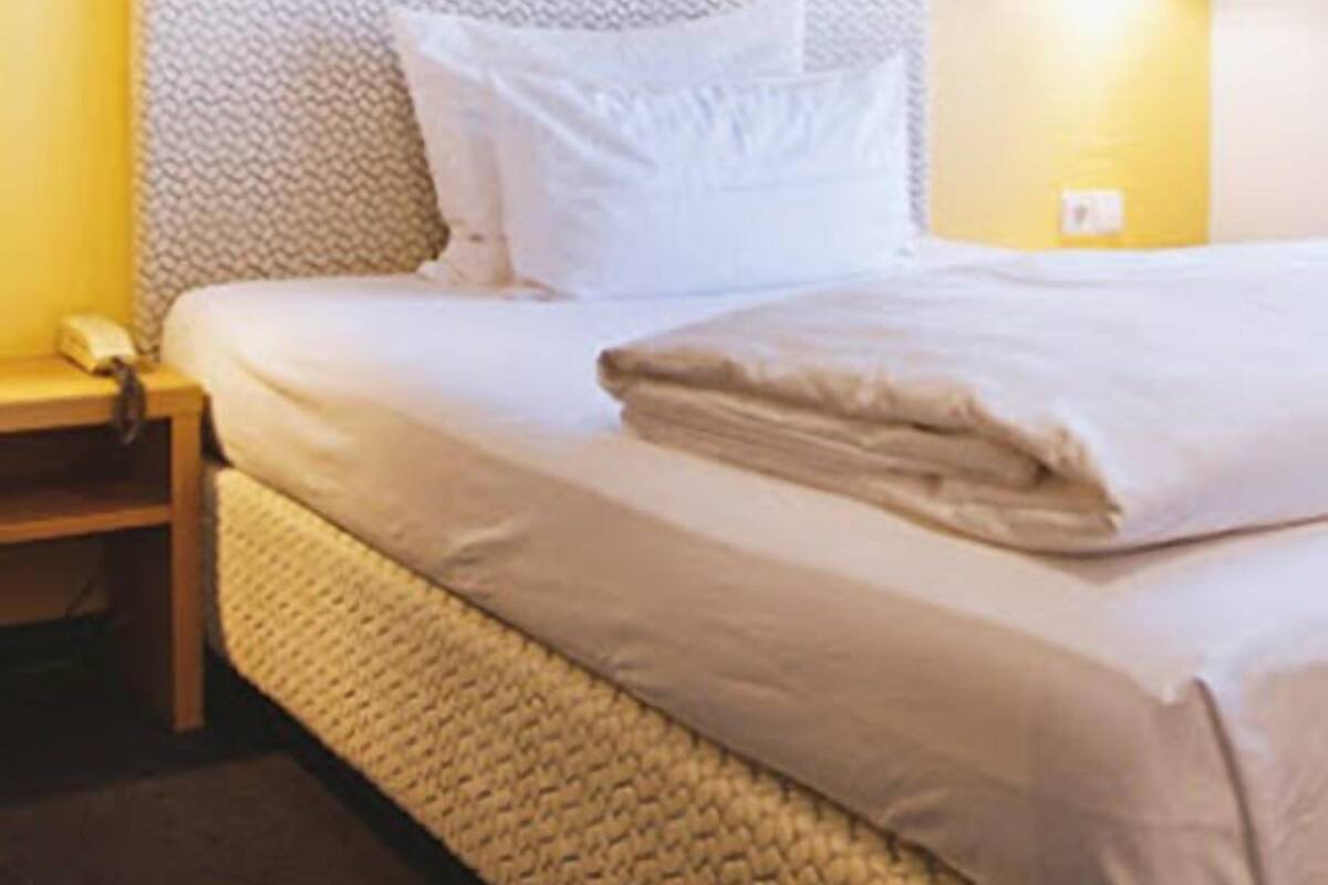 Una cama bien hecha con sábanas blancas, cabecera y una obra de arte colgada en la pared.