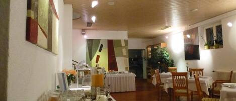 A dining area with tables set for meals, a buffet with food and drinks, and artwork on the walls.