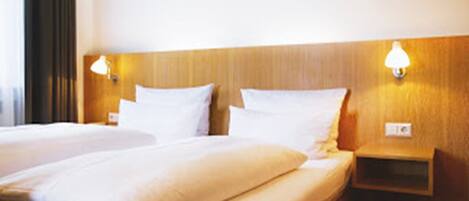 A hotel room with two beds, wooden headboards, bedside lamps, and a nightstand.