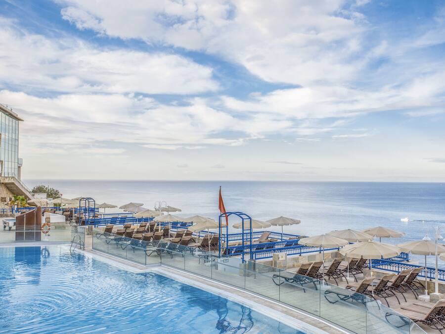 Zona de piscina con sillas de descanso y sombrillas, con vista al mar.