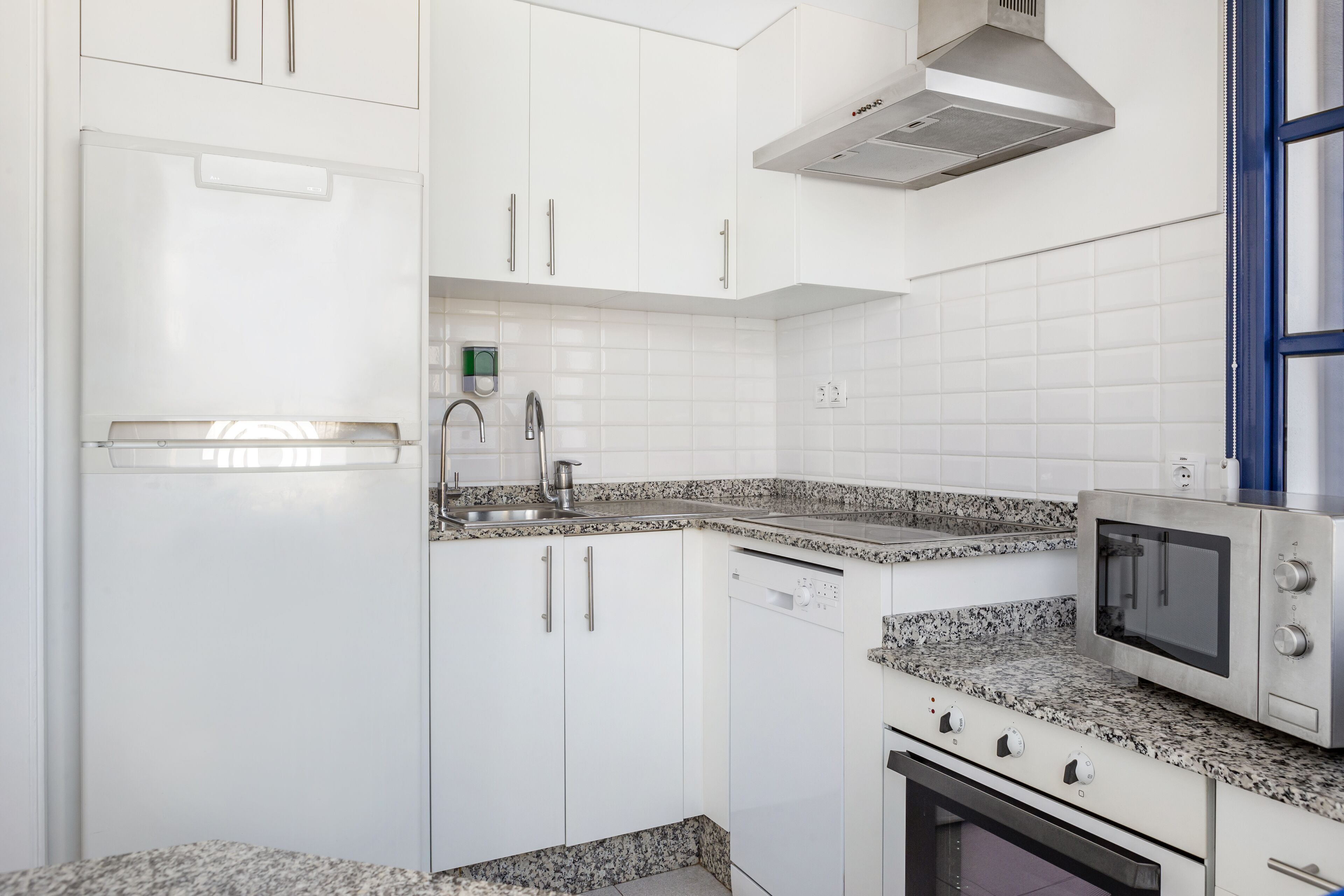 A modern kitchen with white cabinets, a granite countertop, a built-in dishwasher, a microwave, and a stove.