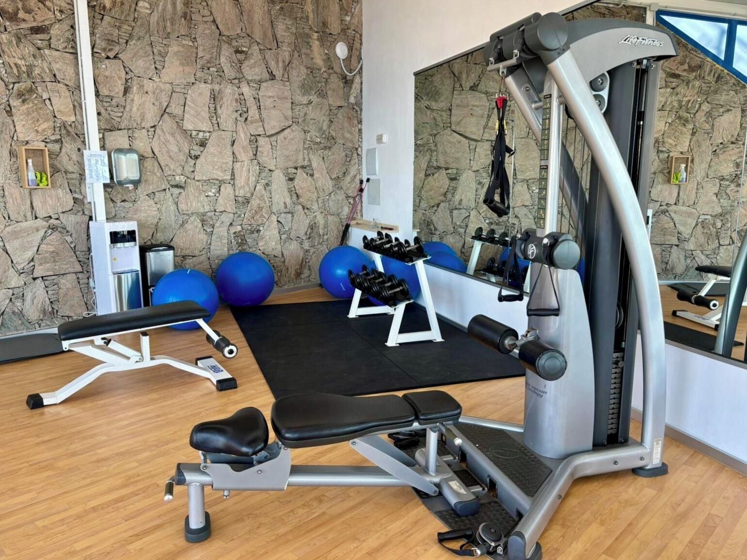 Un gimnasio con pared de piedra, equipo de ejercicio y pelotas de ejercicio azules.