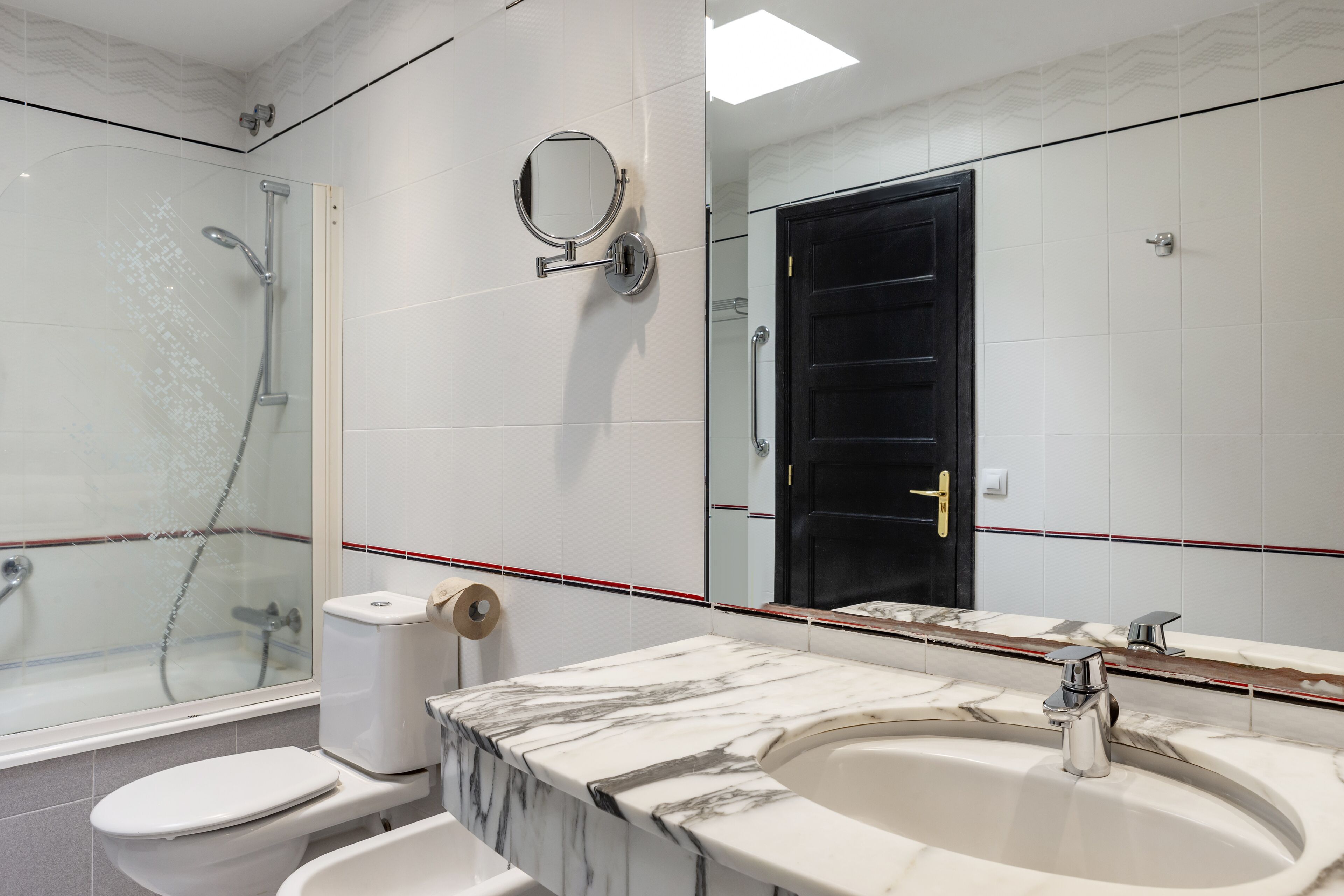 A modern bathroom with a glass-enclosed shower, a toilet, a sink with a marble countertop, and a large mirror.