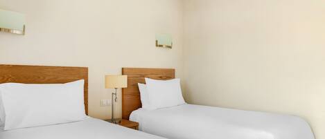 A hotel room with two beds, wooden headboards, and bedside tables with lamps.