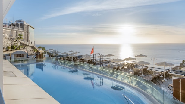 A rooftop infinity pool with a view of the ocean, sun loungers, and umbrellas.