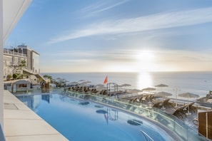 A rooftop infinity pool with a view of the ocean, sun loungers, and umbrellas. - Club Cala Blanca (Mogan)