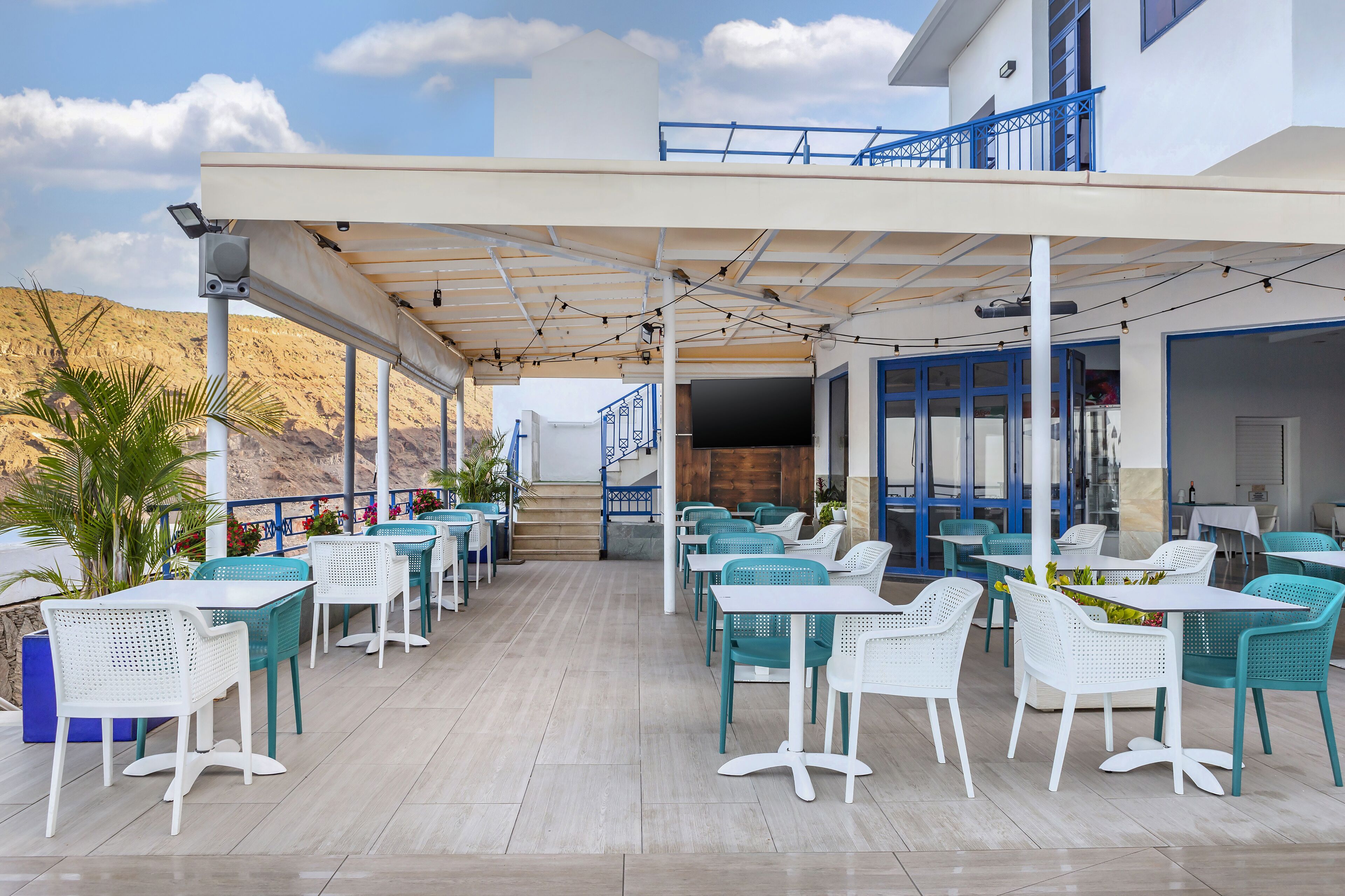 An outdoor seating area with tables and chairs, a covered walkway, and a view of the surrounding landscape.