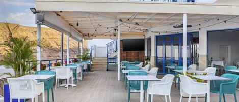 An outdoor seating area with tables and chairs, a covered walkway, and a view of the surrounding landscape.