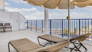 A balcony with two lounge chairs, a table, and an umbrella.