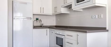 Una cocina moderna con armarios blancos, horno empotrado, microondas y refrigerador de acero inoxidable.