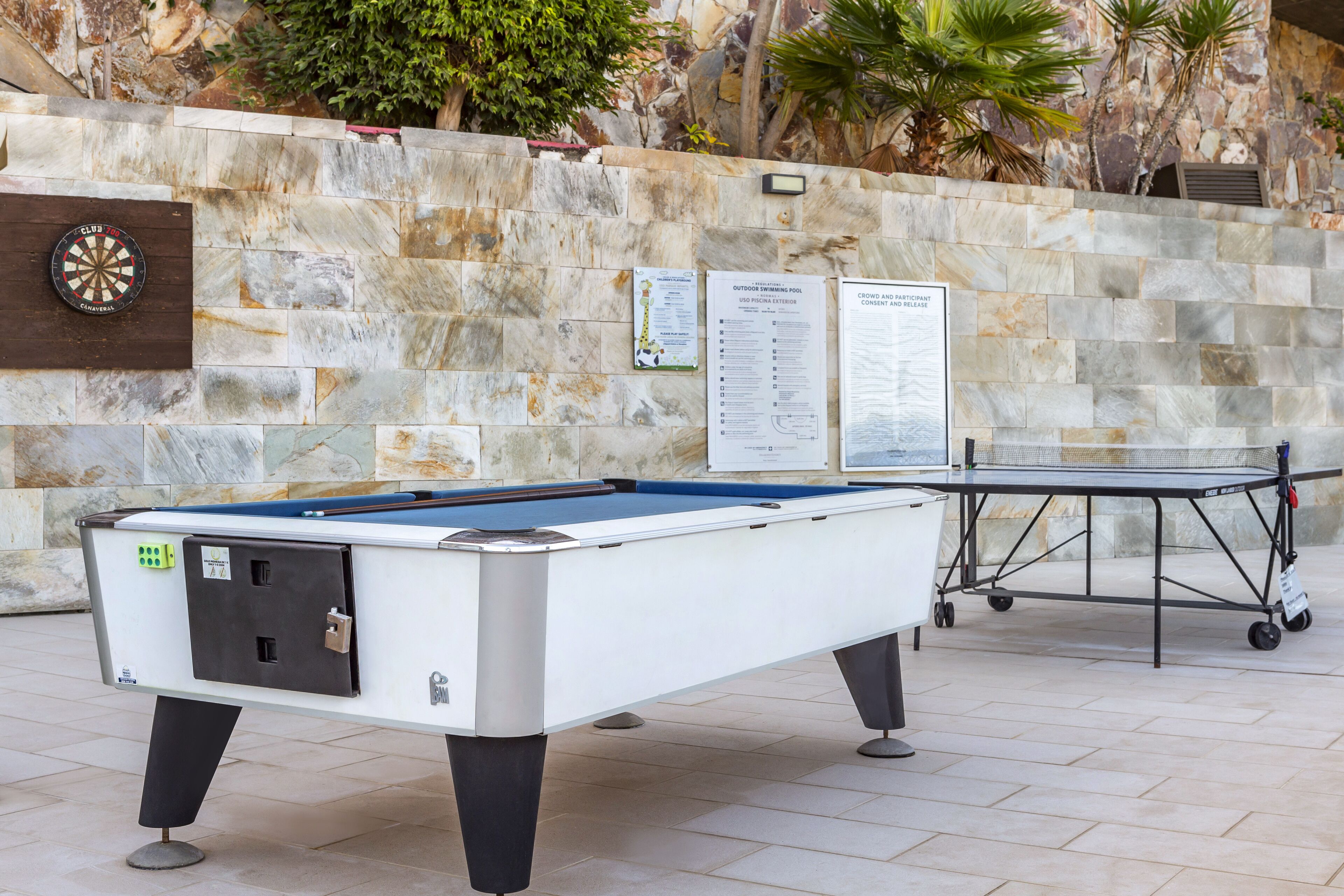 Une table de billard, un jeu de fléchettes et un panneau d’affichage, le tout installé dans un espace délimité par des murs en pierre.