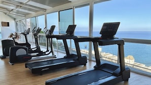 A gym with treadmills and exercise equipment, large windows, and a view of the sea.