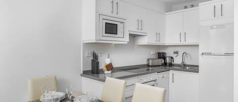A modern kitchen with white cabinetry, a built-in microwave, and a dining area set for four with a table, chairs, and glassware.