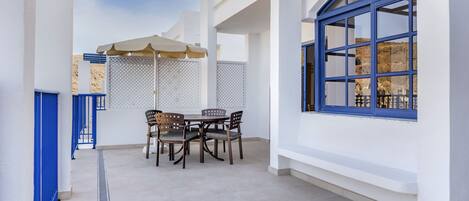 Un amplio patio con mesa y sillas, una pérgola con vigas azules y un ventanal con marco azul.