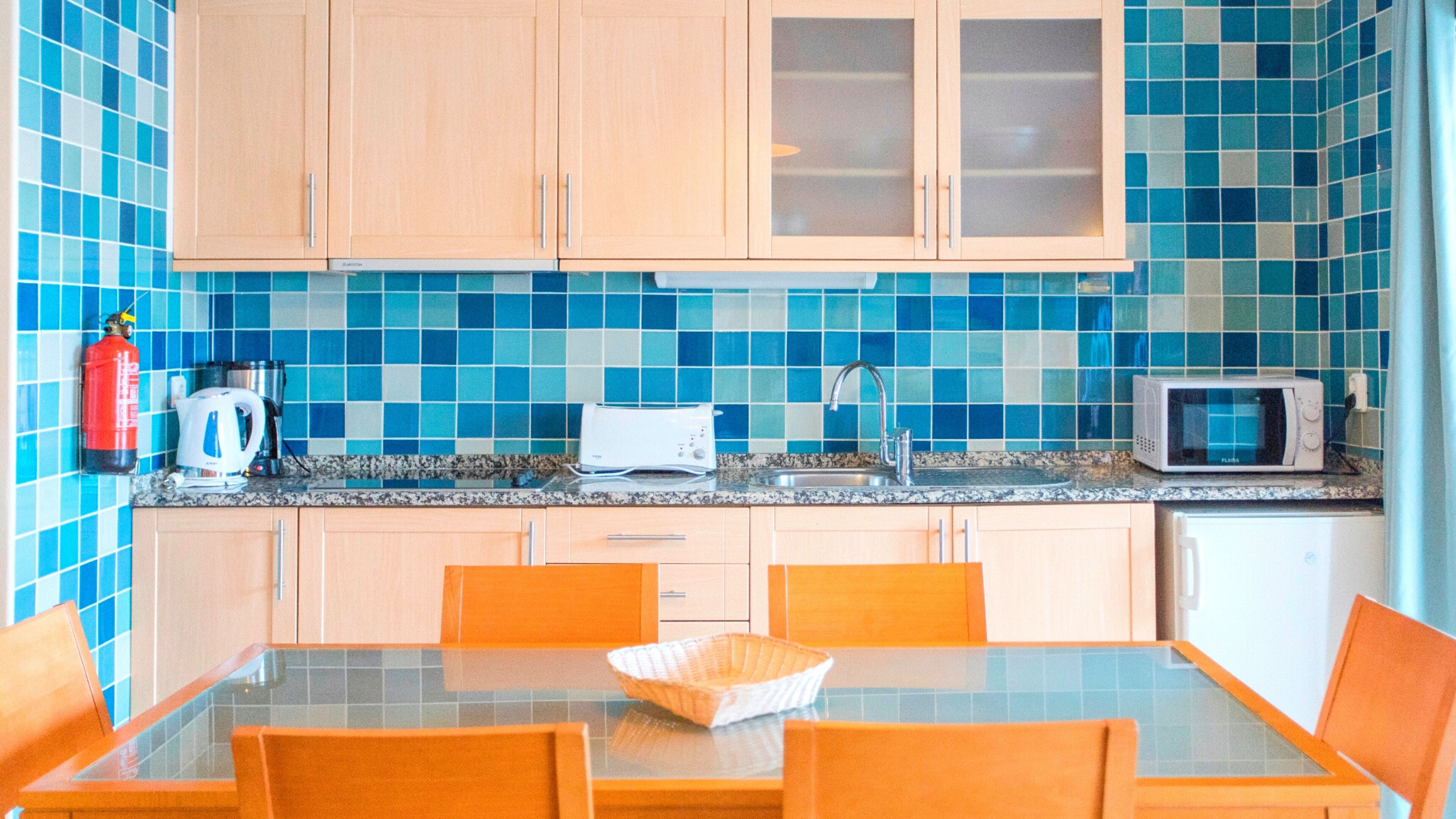 Una cocina con salpicadero de azulejos azules, armarios de madera, microondas, tostadora y cafetera.