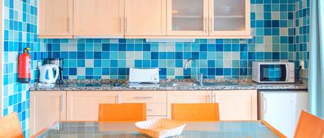 Una cocina con salpicadero de azulejos azules, armarios de madera, microondas, tostadora y cafetera.