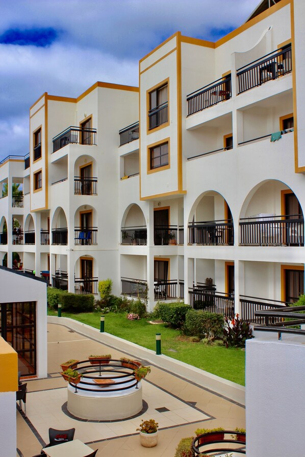 A multi-story hotel with balconies, a central courtyard with seating, and a well-maintained lawn.