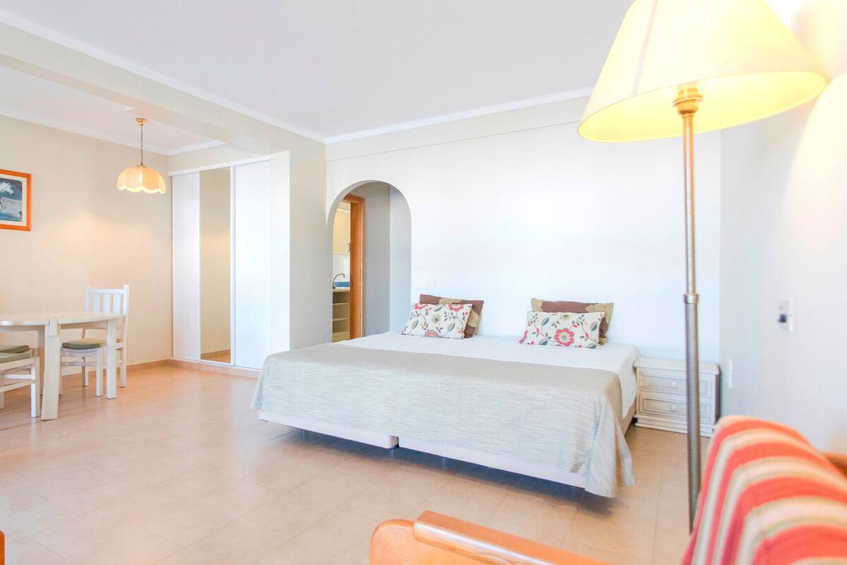 A bedroom with a bed, a desk, chairs, and a lamp.