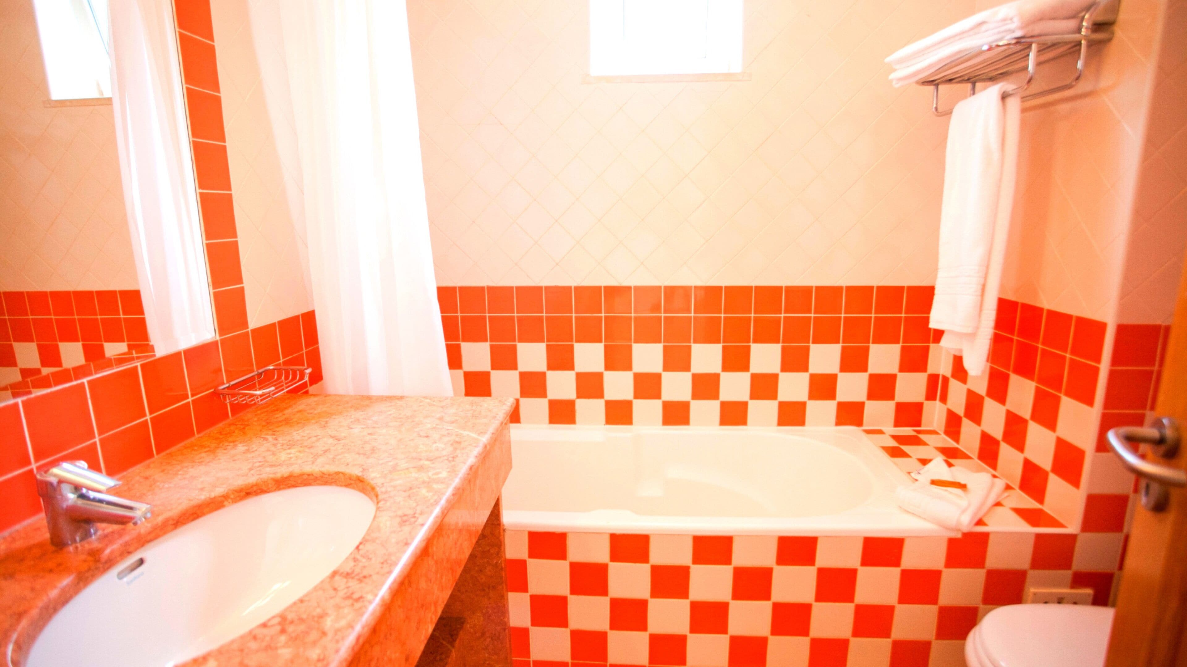 A bathroom with a checkered tile wall, a white bathtub, and a sink with a faucet.