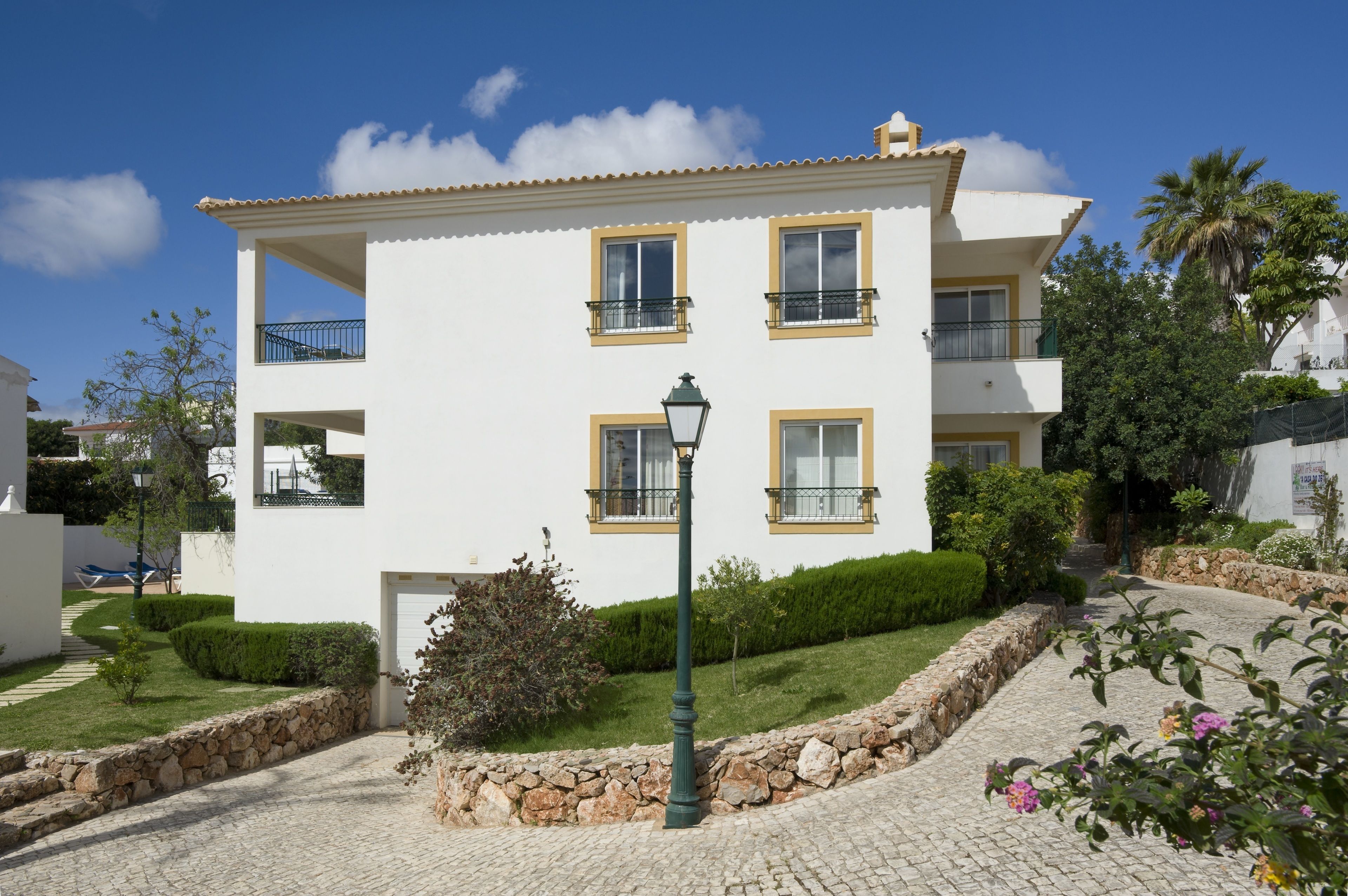 A two-story building with balconies, a paved driveway, and a stone wall.