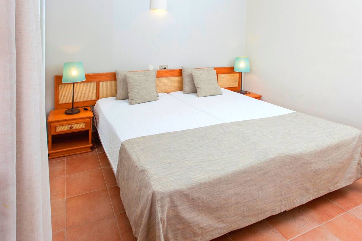 A neatly made bed with a wooden headboard, two bedside lamps, and a nightstand with a lamp.