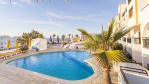 A swimming pool with lounge chairs and umbrellas, surrounded by palm trees and buildings. - Alfagar Cerro Malpique (Albufeira)