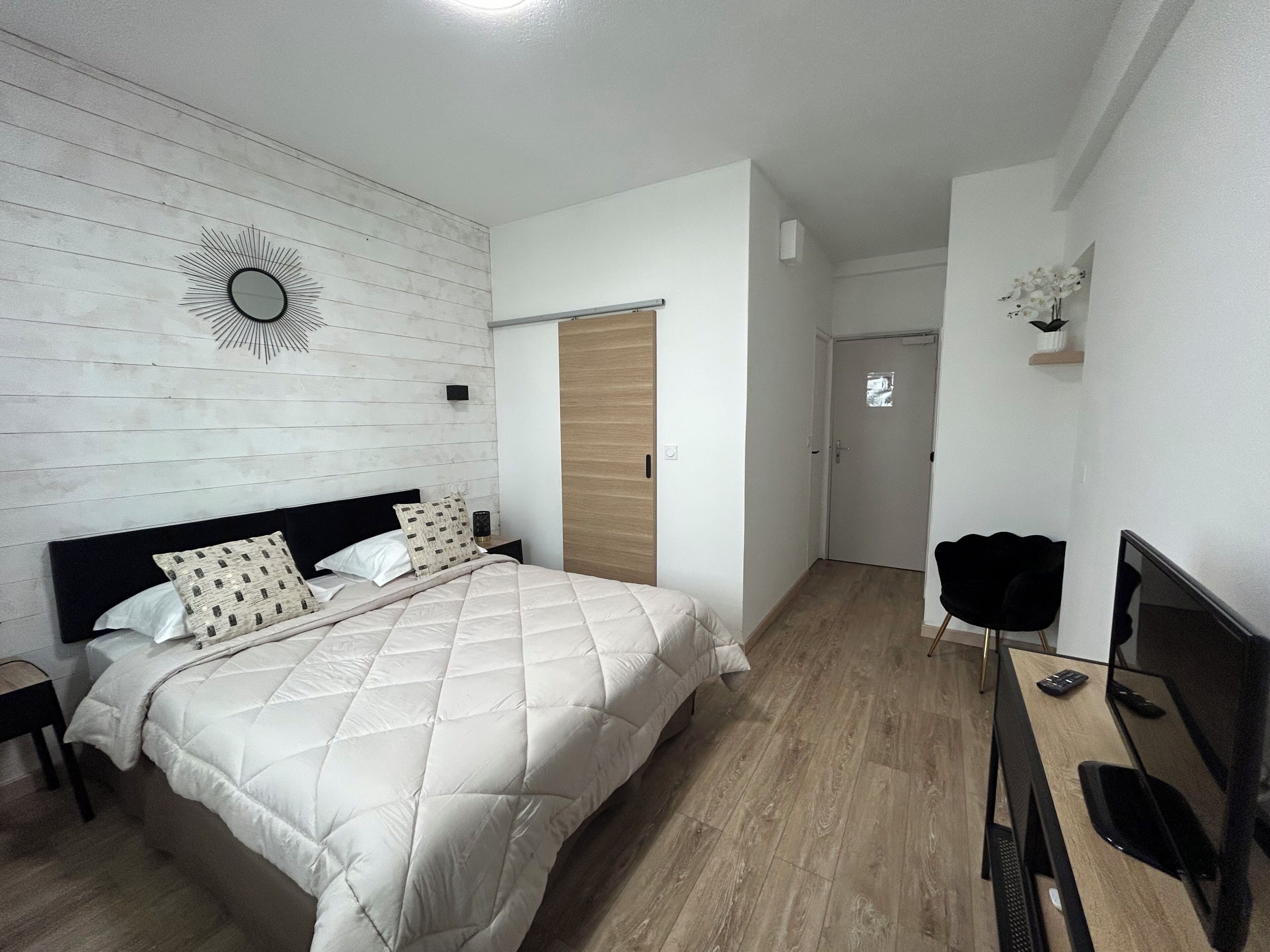 Een slaapkamer met een bed, een televisie, een houten deur en een spiegel aan de muur.