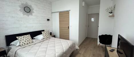 Ein Schlafzimmer mit einem Bett, einem Fernseher, einer Holztür und einem Spiegel an der Wand.