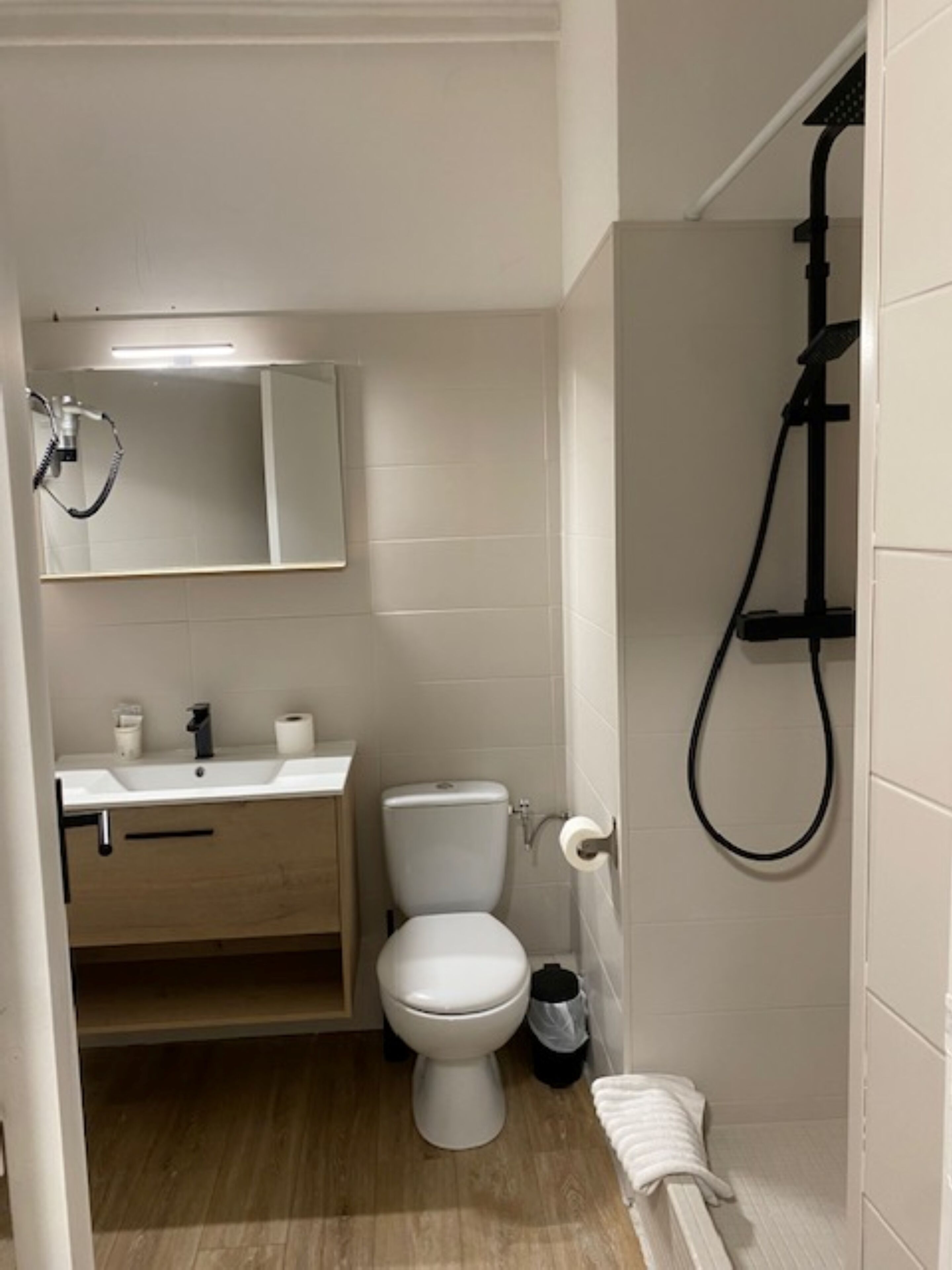 A bathroom with a toilet, sink, mirror, and shower.