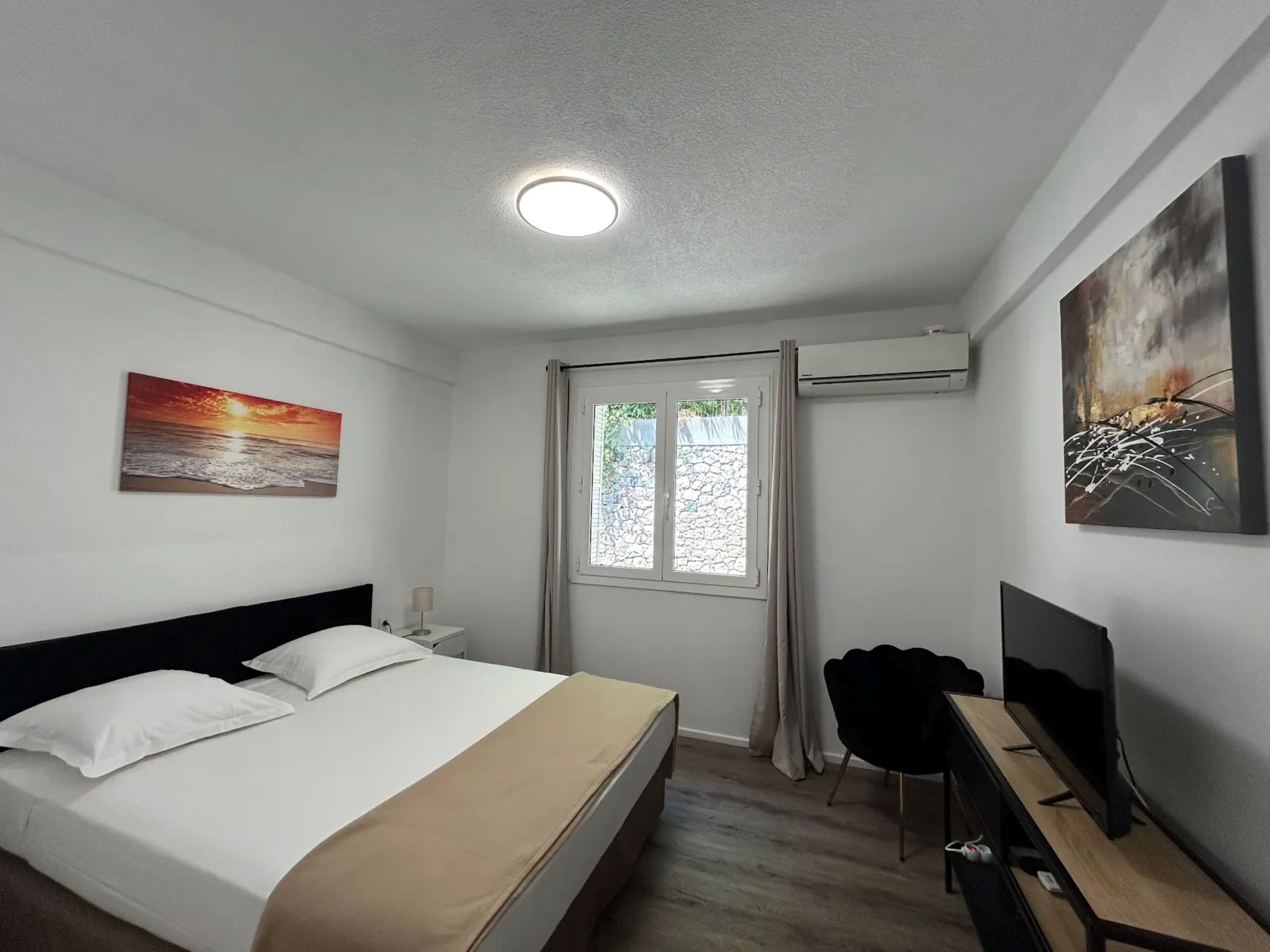 Een hotelkamer met een bed, een bureau, een stoel, een televisie, een schilderij en een raam.