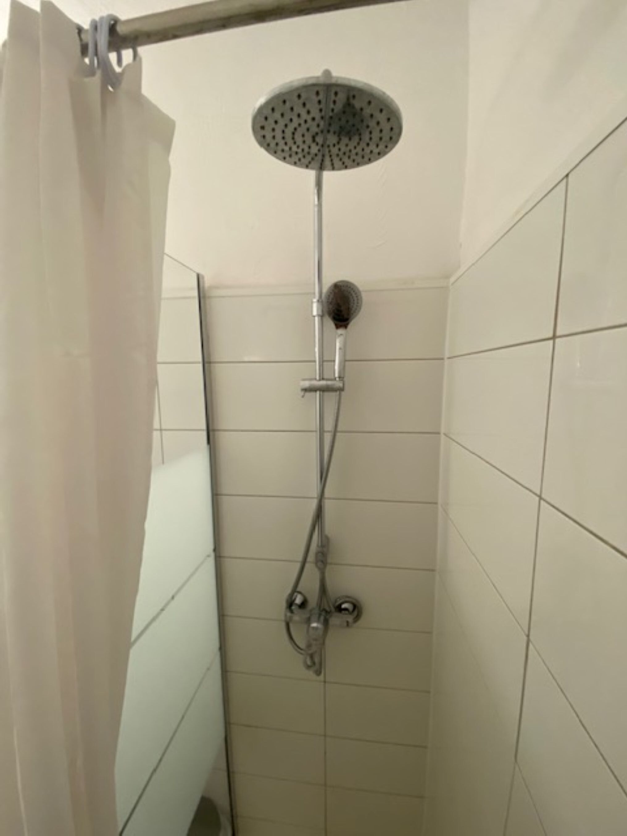 A shower with a handheld showerhead, a wall-mounted rain showerhead, and a curtain.