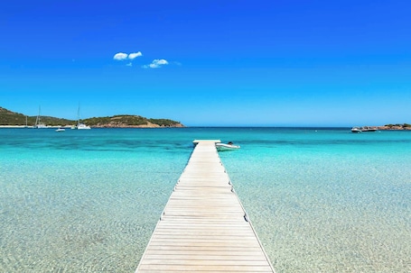 Una banchina di legno si protende in un mare cristallino e blu, con imbarcazioni ancorate nelle vicinanze.. Hôtel Aiglon Bylitis