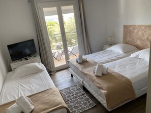 A hotel room with two beds, a TV, a balcony with a table and chairs, and a patterned rug.