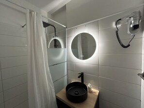 Un baño con cortina de ducha, un espejo redondo, un lavabo con lavamanos negro y un teléfono instalado en la pared.