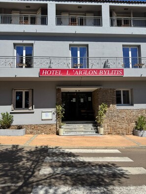 A two-story building with a sign reading "HOTEL L'AIGLON BYLITIS". There are balconies with metal railings, windows with shutters, and a stone facade. - Hôtel Aiglon Bylitis (Porto-Vecchio)