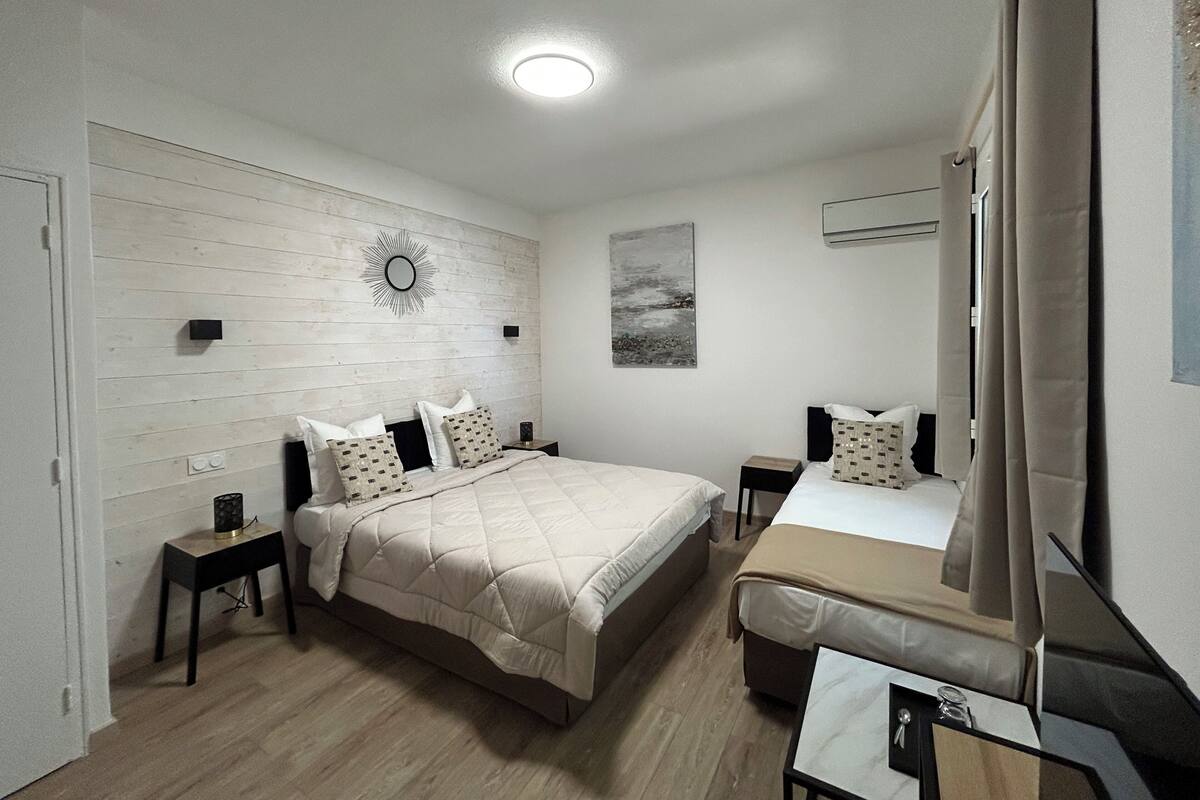 Une chambre à coucher comprenant un lit, des tables de chevet, un miroir et un climatiseur fixé au mur.