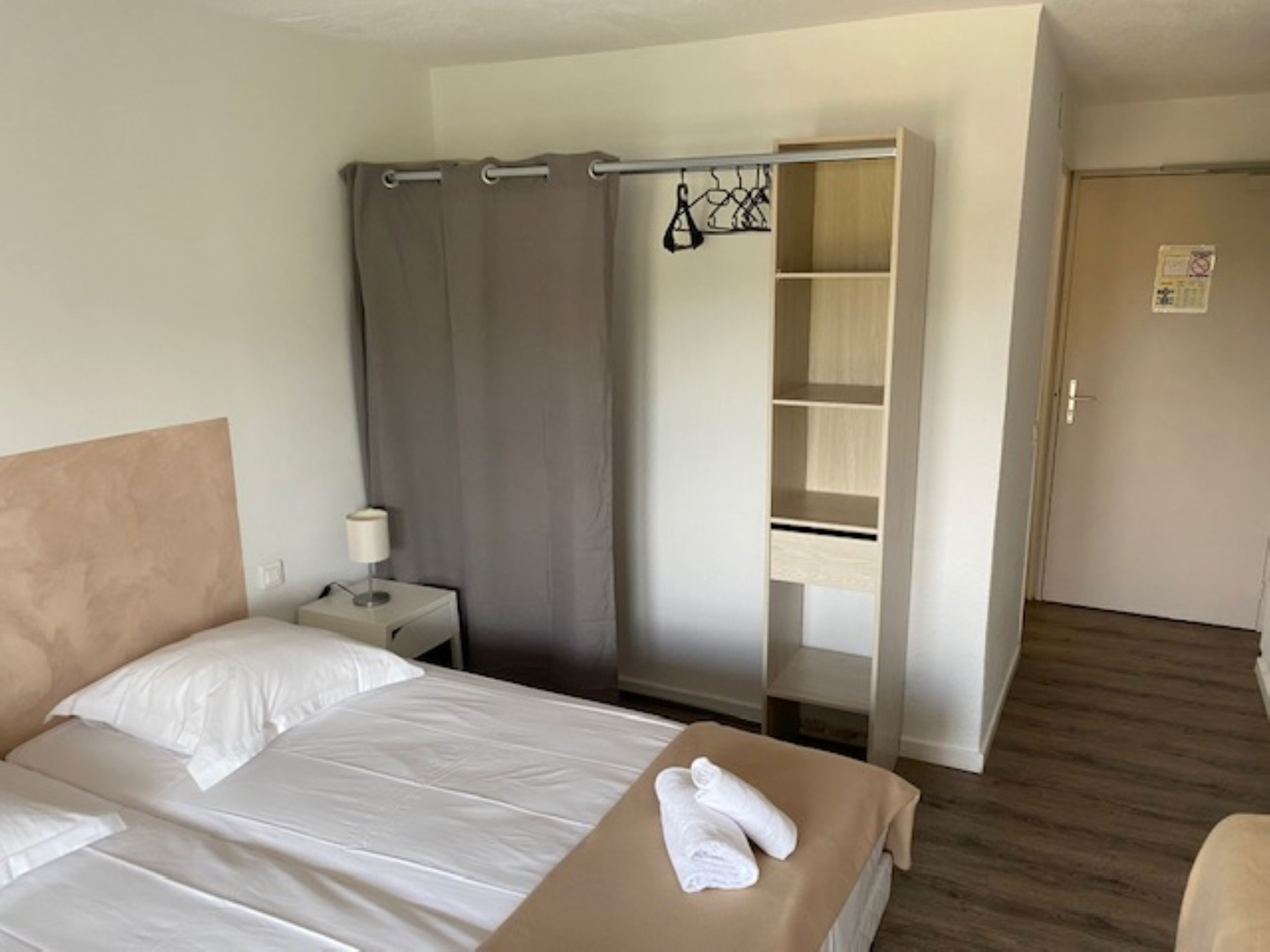 Una camera d'albergo con un letto, un comodino, una scrivania, un armadio e una porta.