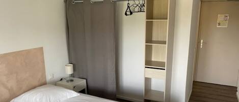 Una habitación de hotel con una cama, una mesita de noche, un escritorio, un armario y una puerta.
