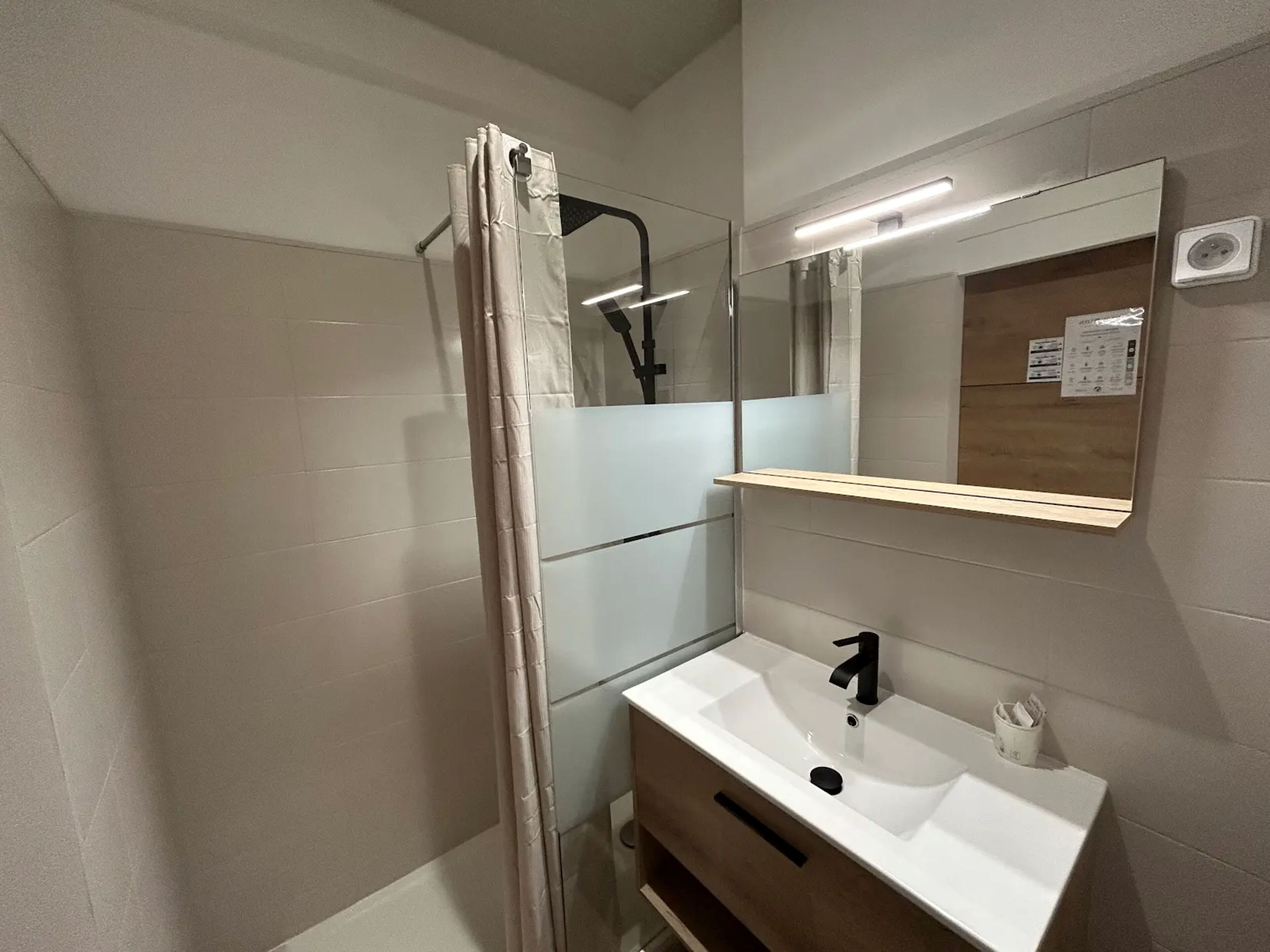 A bathroom with a shower, a sink, a mirror, and a light fixture.