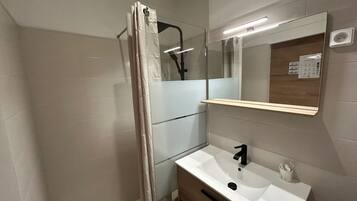 A bathroom with a shower, a sink, a mirror, and a light fixture.